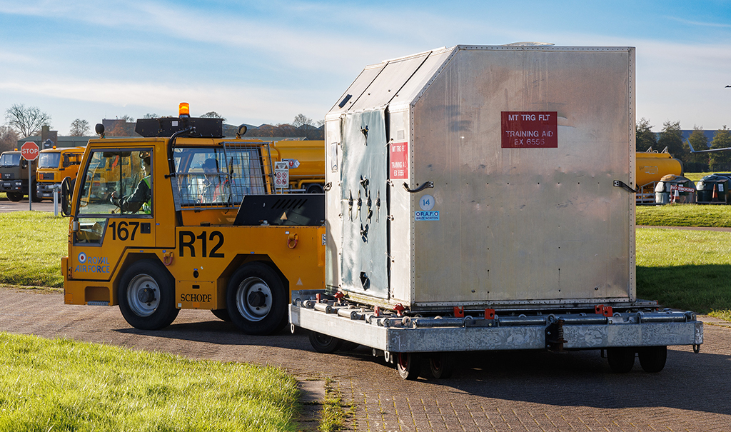 Photo: Airfield vehicle being driven during the Maneuvering Training event. The vehicle is towing a trolley laden with an aircraft baggage container.